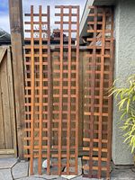 Three stained cedar lattice panels standing upright outside against a fence and wall, showing overall size and color differences.