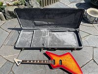 Open guitar case with electric guitar body inside, showing sunburst finish and fretboard.