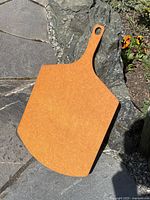 Full view of the pizza oven paddle showing shape and color, placed outdoors on stone surface