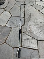 Full view of the extendable aluminum wand fully extended and laid flat on stone surface showing the entire length and handle.