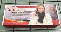 Front photo of the HeatMatez heated scarf box showing product name, image of person wearing scarf, and key features including 3 adjustable heat levels and USB power source.