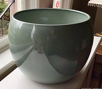 Front view of large celadon ceramic plant pot showing glossy light green glaze and rounded shape.