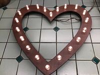 Heart shaped marquee light with 20 lit globe bulbs resting on tiled floor, showing full item and bulb layout.