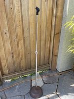 Full length view of vintage metal microphone stand with weighted base and plastic microphone holder top, set against wooden fence background.