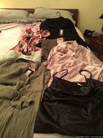 All clothing items laid out on bed including floral overblouse and palazzo pants, black satin cami, crinkled blouses, jeans and shorts.
