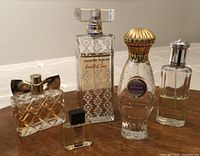 Five perfume bottles arranged side by side on a wooden table. Various levels of perfume content visible