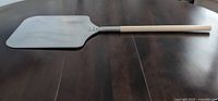 Full view of pizza paddle on table showing wooden handle and metal paddle head.
