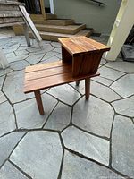 Angled side view showing stepped design with smaller upper level and larger lower level supported by four wood legs.