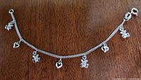Sterling silver chain bracelet with small silver-toned baby-themed charms hanging at intervals, including hearts and baby figures, laid flat on wooden surface.
