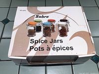 Closed box labeled 'Sabre Spice Jars' showing image of jars with colored lids on tiled surface.