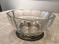 Clear octagonal thick glass bowl with faceted sides, sitting on a round silver metal base. Photo taken from side angle showing form and thickness of glass.