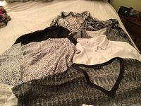 First photo showing a variety of light and dark colored tops including animal prints, patterns, and solid colors laid out on a bed.