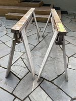 Two handmade solid wood sawhorses shown standing on a stone patio, displaying structure and length.