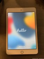 Front view of iPad Mini 4 powered on, showing 'hello' welcome screen.