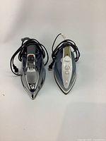 Both vintage clothes irons shown from top-down angle revealing cords, controls and soleplates.