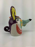 Side view of the face-shaped ceramic tea pot showing the colorful painted facial features, curved handle, and spout nose.