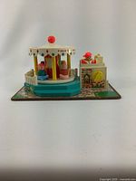 Full frontal view of vintage Fisher Price carousel toy set showing the carousel with three seated figures and the box unit with turning knob on printed base