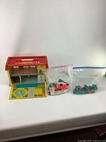 Photo of the complete Fisher Price hospital playset with two sealed bags of small plastic pieces and figures next to it. The playset is open, showing the exterior and interior details.