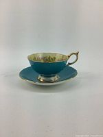 Side angle of turquoise Aynsley teacup with scalloped rim, gold trim on handle and base, showing vintage condition.