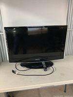 Front view of Samsung TV on table with power cord and remote in front