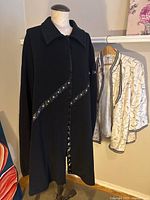 Black wool cape displayed on a mannequin, showing front and collar detail with satin snap button trim in a diagonal pattern.