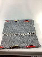 Gray folded wool blanket with colorful bird embroidery and fringed tassels on edges.