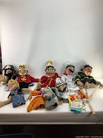 Assorted vintage puppets including Fozzy Bear, pirate, kings, chef, and other characters displayed on white surface with some holding wooden rods.