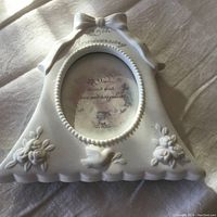 Front view of white ceramic 25th anniversary picture frame featuring decorative bow and sheep with rose flowers on ceramic base, including text detailing.