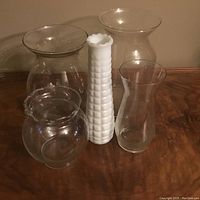 Image showing five flower vases on wooden surface: four clear glass and one white milk glass with textured design