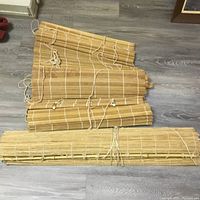 Photo of one large bamboo blind rolled out near floor showing natural bamboo slats and white rolling cords.