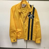Yellow Bardahl jacket hanging, showing front side with black stripes and Bardahl logo patch on chest.