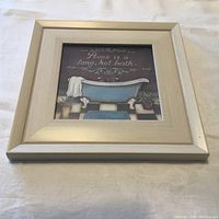 Photo of the framed bathroom wall art displaying a blue clawfoot bathtub with the quote 'Peace is a long, hot bath.'