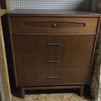 Chest of drawers with four drawers in light wood finish, metal handles, and a round knob on the top drawer.