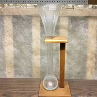 Front view of the Dutch beer glass placed vertically in the wooden stand on a wooden surface against a soft textured background.