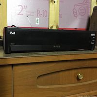 Photo shows Bell HDTV 6500 dish console sitting on a wooden surface with pink insulation foam board in the background.