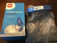 Photo showing Life Unisex Urinal in its box next to a clear waterproof cast and bandage protector with blue seal ring.