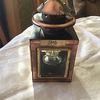 Front view of copper lantern with glass window and brass frame, showing wick holder inside and copper vented top.