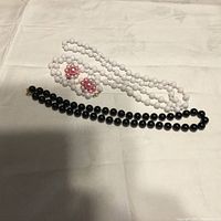 White bead necklace, black bead necklace, and pink pearl cluster earrings laid out on a white fabric background.