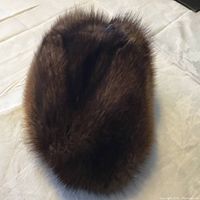 Top view of a brown fur hat laid flat on a cream surface showing dense fur texture and rounded shape, indicating winter use.