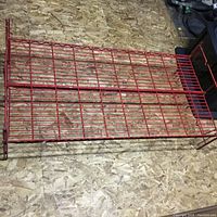 Red iron hospital bed frame laid flat on oriented strand board floor, showing bars and frame structure
