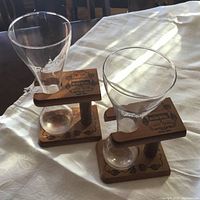 Two Kwak beer glasses placed upright in their wooden stands on a white tablecloth, showing the characteristic bulbous bottom of the glasses and the branding on the stands.
