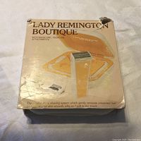 Box front of Lady Remington Boutique shaver showing product image and text in English describing its shaving system and attachments.
