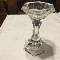 Front view of a large clear crystal candle holder with hexagonal base and top, placed on a white cloth.