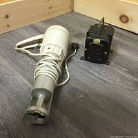 Photo of an electric handheld meat grinder and a black electrical power converter box placed on a wooden surface.