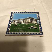 Photo of the square ceramic plate with Parthenon image and Greek key border taken on a white cloth surface.