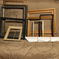 Multiple picture frames of different sizes and colors arranged on a sofa. Frames include black, gold, natural wood, and white decorative types, some with hanging strings attached.