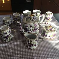 Full tea set including teapot, creamer, sugar bowl with lid, and six cups arranged on tablecloth.