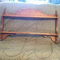 Wooden shelf unit with decorative carved details, two horizontal shelves with slots designed to hold decorative plates securely in place. Medium brown wood, vintage style, approx. 24x37 inches.