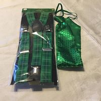 Green plaid suspenders in packaging, solid green tie, and green sequin tie lying flat on a surface.