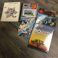 Photo showing five unopened sympathy stamp collection books and single packs from 1987 to 1992 on wood floor.